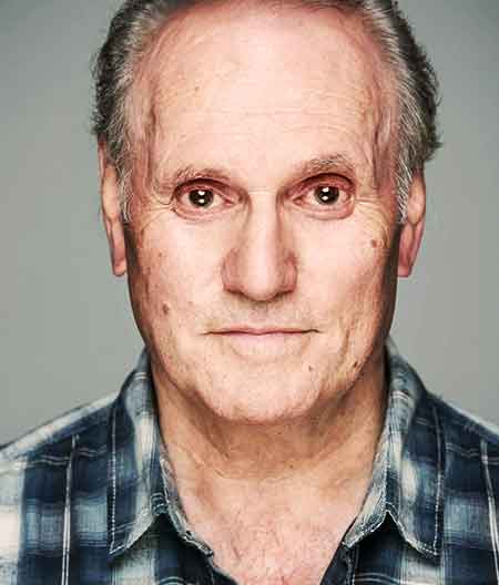 close up view of sean glenn in a blue and light blue checked shirt wearing a very menacing facial eexpression